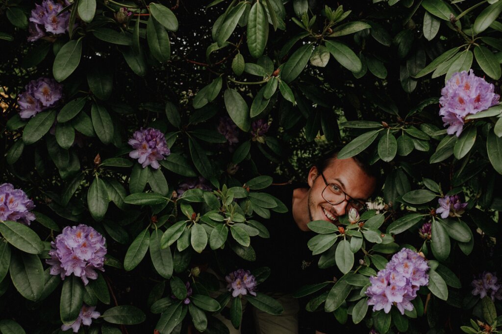 Statamic developer Johannes Schuba stands in a large plant in the garden and laughs into the camera.